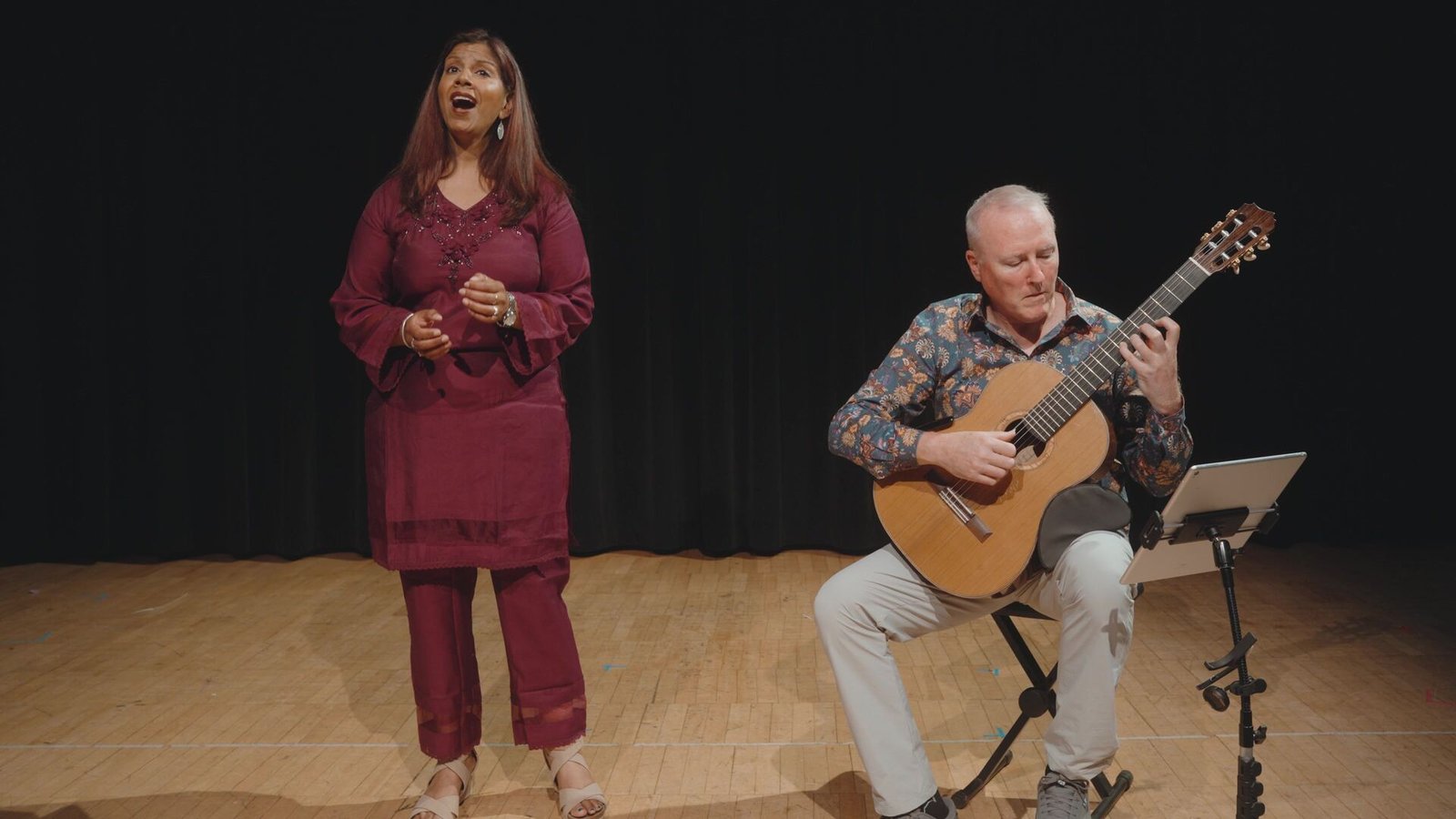Abha Dearing singing on stage while Steven Dearing plays classical guitar